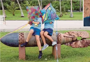  ?? AGENCY PIX ?? Pupils sitting on the remants of a World War 2 bomb at Asan Memorial Park in Guam on Friday. Residents are more afraid of typhoons than a North Korean missile attack by Kim Jong-un (inset).