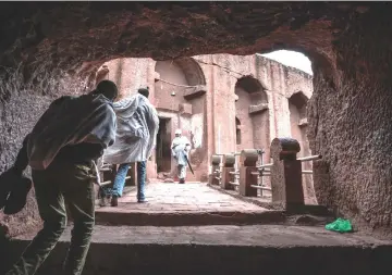  ??  ?? (Left) An Ethiopian Orthodox priest Mekonnen Fatne (right) near the church of Saint Mary which is covered by a shelter to protect its rock-hewn structure from erosion. • (Right) Ethiopian Orthodox devotees walk between the rock-hewn churches of Saint Gabriel and Saint Raphael in Lalibela. — AFP photos