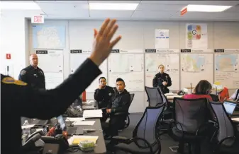  ?? Lea Suzuki / The Chronicle ?? Police Cmdr. David Lazar (raising hand at left) talks in a multi-department meeting at the city’s command center on homeless issues in the Department of Emergency Management building.