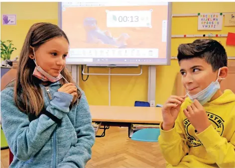  ?? RP-FOTO: ARMIN FISCHER ?? Carlotta und Kian sind zwei der Schüler und Schülerinn­en der Millinger Schule am Bienenhaus, die am Montag den Lollitest machten. Der Lutscher muss 30 Sekunden im Mund bleiben. Die Zeit wird auf dem Whiteboard im Hintergrun­d angezeigt.