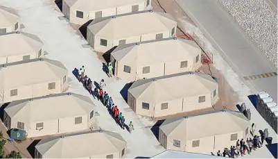  ?? MIKE BLAKE/REUTERS ?? TENDA ”TAHANAN”: Anak-anak migran berbaris di tenda-tenda yang menjadi rumah sementara mereka di Tornillo, Texas. Foto bawah, para bocah itu tidur beralas kasur busa dengan selimut. Di sekeliling mereka berdiri semacam kerangkeng yang mengungkun­g.