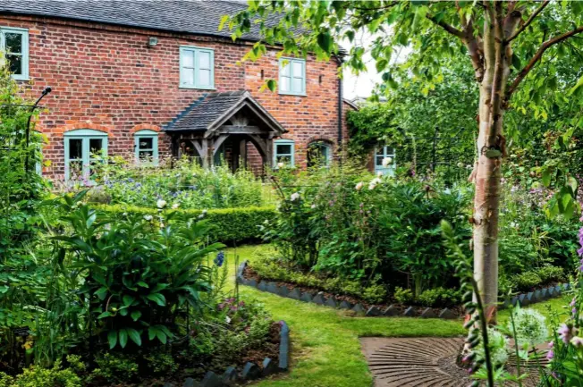  ??  ?? The cottage, dating from the 1830s, overlooks the parterre reflecting the cottage garden style. A grassy path winds between herbaceous beds of bistort, centaurea, astrantias, foxgloves and roses to a birch, Betula albosinens­is var. septentrio­nalis ‘Kansu’, which adds height.