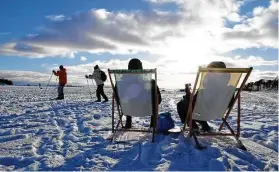  ?? Jussi Nukari / Associated Press ?? People sit in the sunshine as others ski by during a sunny winter day on waterfront ice in Helsinki last month. Finland was ranked the happiest country in the world.