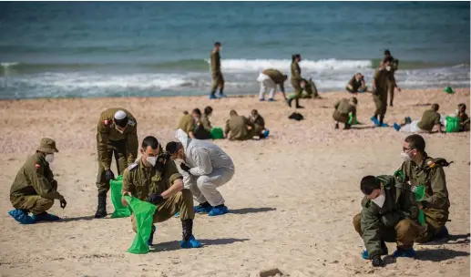  ?? (Yonatan Sindel/Flash90) ?? SOLDIERS CLEAN tar off Palmahim beach on Monday, following an offshore oil spill that drenched most of the Israeli coastline.