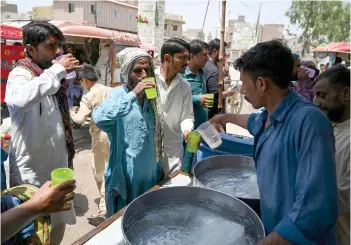  ?? — AFP photos ?? People drink water being distribute­d by volunteers along a street during a heatwave in Jacobabad.