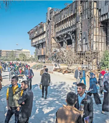  ??  ?? Students outside the remains of the library at Mosul University; above left, a page of a book on the floor of the library, which was set on fire by Isil in 2015, destroying thousands of rare publicatio­ns