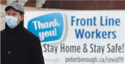  ?? CLIFFORD SKARSTEDT EXAMINER ?? Mitchell Parker walks past a sign thanking front-line workers on George Street on Tuesday. Premier Doug Ford has declared another state of emergency and issued a 28-day “stay-at-home order” that takes effect on Thursday at 12:01 a.m.