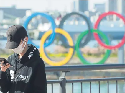  ?? FOTO: AP ?? Un turista con mascarilla en Tokio consulta su teléfono móvil en el distrito olímpico de Odaiba y con los aros de testigo