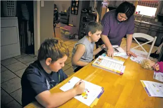  ?? EDMUND D. FOUNTAIN/THE NEW YORK TIMES ?? Jarrett Nelams, 7, and his brother, Jadon, 9, work on English homework with their mother, Rebekah, in 2014 at their home in Greenwell Springs, La. With a little creativity, parents can help kids overcome barriers to homework productivi­ty.