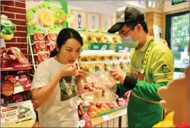  ?? SHEN CHUNCHEN / FOR CHINA DAILY ?? A consumer (left) tastes a new variety of red kiwis at a fruit store in Shanghai in April 2021.