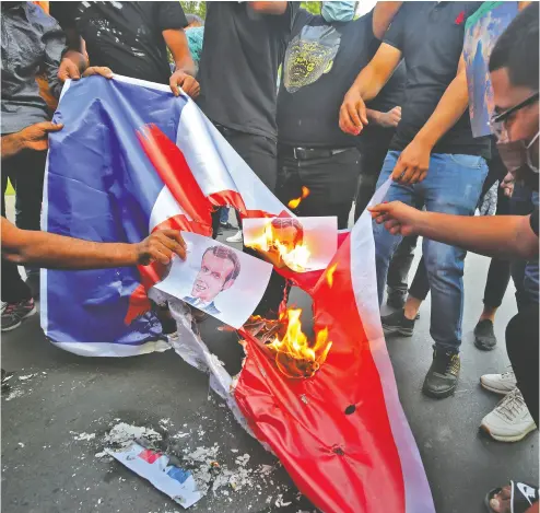  ?? AHMAD AL- RUB AYE / AFP via Gett y Imag es ?? Iraqi protesters burn posters and the flag of France at a demonstrat­ion on Tuesday against French President
Emmanuel Macron in front of the French embassy in Baghdad.