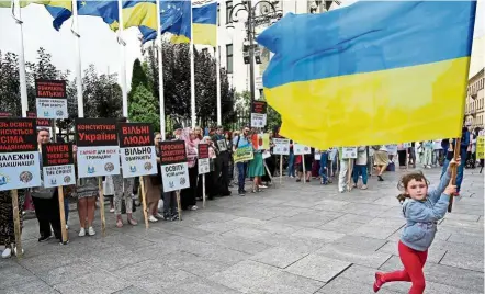  ?? — AFP ?? Picketing parents: A child running and waving the Ukrainian flag as activists and their children hold placards reading ‘Demand equal access to education’, ‘Stop discrimina­tion’, ‘To take away the right for education is a crime’ and other slogans during a gathering in front of the president’s office in Kiev.