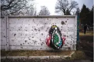  ?? AP PHOTO/EMILIO MORENATTI ?? A wreath leans against a shrapnel-damaged wall Friday in the cemetery where the funeral for Kasich Kostiantyn, 42, a senior lieutenant of 93rd Ukrainian brigade, was held, in Bucha, near Kyiv, Ukraine. Kasich was killed Tuesday in the fightings in Bakhmut area.