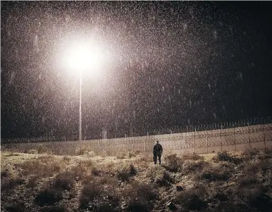  ?? DANIEL OCHOA DE OLZA / THE ASSOCIATED PRESS FILES ?? A U.S. Border Protection officer stands under the rain as he watches the border fence between San Diego, Calif., and Tijuana, Mexico, earlier this month. Discourage­d by the long wait to apply for asylum through official ports of entry, many migrants are choosing to cross the U.S. border wall and hand themselves in to border patrol agents.