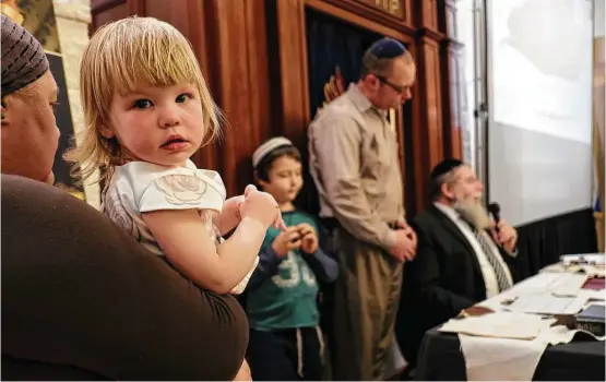  ?? Elizabeth Conley photos / Houston Chronicle ?? Hadassah Levit, 2, is held by her mother, Abigail Neiman, as the family watches Rabbi Heshy Pincus write the first sentence of a new Torah.