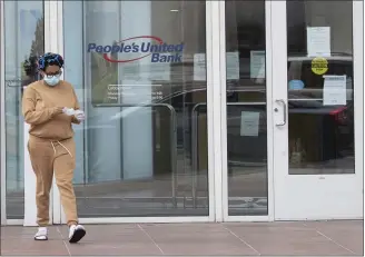  ?? MARY ALTAFFER — THE ASSOCIATED PRESS FILE PHOTO ?? A woman wearing leaves the People’s United Bank in Bridgeport, Conn., after using an ATM. As bank branches remain shuttered, more people are having a go at doing their banking online.