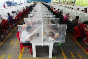  ?? Moises Castillo/Associated Press ?? Workers eat their lunch separated by plastic panels as a measure against the spread of the coronaviru­s Friday at K.P. Textil in San Miguel Petapa, Guatemala.