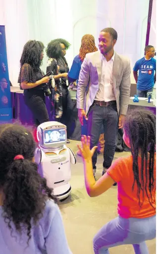  ?? PHOTO BY FRANCINE BUCHNER ?? School age child tests the capabiliti­es of GlobalDWS’s Teacher’s Assistant robot. The first of it’s kind in the world. Standing beside robot: Dwayne Matthews, education consultant, GlobalDWS.
