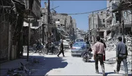  ?? HASSAN AMAR / ASSOCIATED PRESS ?? People walk Monday among damaged buildings in the town of Douma, the site of a suspected chemical weapons attack near Damascus. Syrian troops earlier declared the town liberated from opposition fighters.