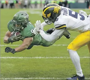  ?? KENNETH WALKER Al Goldis Associated Press ?? dives over the goal line past Michigan’s DJ Turner in the second quarter. Walker’s fifth score was the game-winner as the Spartans knocked off their rival.