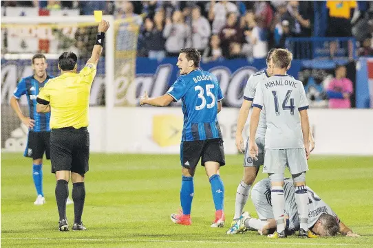  ?? THE CANADIAN PRESS ?? Deian Boldor of the Impact, centre, is shown the yellow card for a hit on Bastian Schweinste­iger that left the Fire midfielder writhing in pain on the turf.