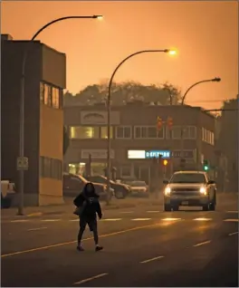  ?? The Canadian Press ?? A woman walks across a street just after 10 a.m. in near darkness due to thick smoke blanketing the city because of wildfires in the region, in Prince George, B.C., on Friday.