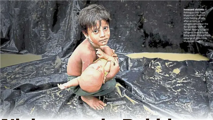  ?? — AFP ?? Innocent victims: A Rohingya child from Myanmar’s Rakhine state holding a baby after arriving at a refugee camp near the Bangladesh­i town of Teknaf. Nearly 125,000 refugees have entered Bangladesh since a fresh upsurge of violence in Myanmar.