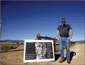  ?? DAN ELLIOTT — THE ASSOCIATED PRESS ?? Stephen Parlato wears a gas mask next to his sign warning about the dangers of plutonium at Rocky Flats National Wildlife Refuge outside Denver on Saturday the first day the refuge was open to the public. The refuge is on the outskirts of a former U.S. government factory that manufactur­ed plutonium triggers for nuclear weapons.