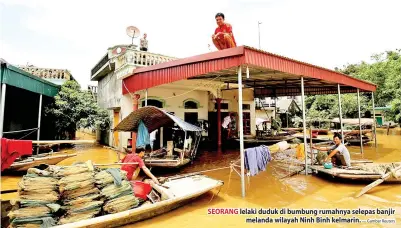  ?? — Gambar Reuters ?? SEORANG lelaki duduk di bumbung rumahnya selepas banjir melanda wilayah Ninh Binh kelmarin.