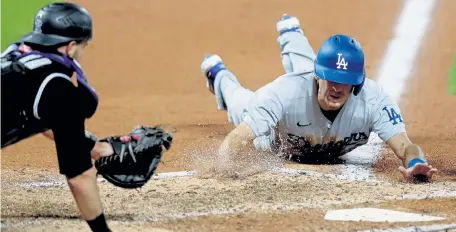  ?? Matthew Stockman, Getty Images ?? Austin Barnes of the Los Angeles Dodgers scores against Colorado catcher Drew Butera on a wild pitch in the seventh inning Saturday night at Coors Field.