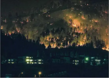  ?? AP FILE ?? The Mcdougall Creek wildfire burns Aug. 18 on the mountainsi­de above houses in West Kelowna, British Columbia. Wildfires are bringing fresh scrutiny to Canada’s fossil fuel dominance, its environmen­tally friendly image and the viability of becoming carbon neutral by 2050.