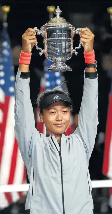  ?? /Julian Finney/Getty Images ?? Calm and collected: Naomi Osaka hoists the trophy after her historic win at the US Open.