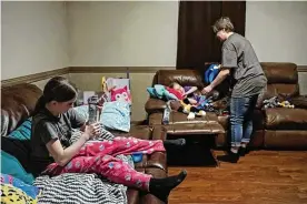  ?? JOSEPH SCHELLER / COLUMBUS DISPATCH ?? Misty Kalcevic tucks in her 6-year-old daughter, Chloe, while Kalcevic’s other daughter, 11-year-old Jaycee, opens a bottle of water Thursday night in their East Palestine home. Partly due to a smell present in their bedrooms, Kalcevic has had her daughters sleep in the living romm out of concern that their belongings and mattresses have absorbed chemicals released by the train derailment.