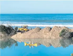  ?? Picture: RICHARD ARDERNE ?? CALM FOR NOW: A Kouga Municipali­ty team uses front-end loaders to push sand into the breach in the sand spit separating Ski Canal from the sea at St Francis Bay yesterday