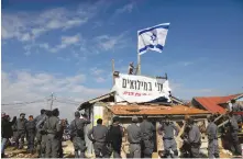  ?? (Ronen Zvulun/Reuters) ?? A SETTLER STANDS atop a structure, surrounded by police, with a banner that reads ‘I am in the military reserves,’ in the Netiv Ha’avot outpost in Gush Etzion in November.