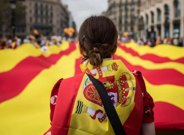  ??  ?? TRUE COLOURS: A woman wearing a Spanish flag on her shoulders looks at a giant flag of Catalonia as people celebrate a holiday known as Dia de la Hispanidad, or Spain’s National Day, in Barcelona last Thursday, amid one of the country’s biggest crises...