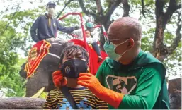  ?? ALLEX QOMARULLAH/JAWA POS ?? LAWAN KORONA: New Man memasangka­n masker kepada anak yang sedang berkunjung ke Kebun Binatang Surabaya.