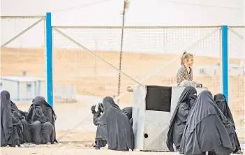  ?? ?? Women and children sit next to a metal container along a fence.