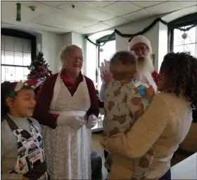  ?? ?? Mr. and Mrs. Santa Claus, played by Ben and Amy Schiavone of Exeter Township, greet a young resident of Opportunit­y House, held by volunteer Jana Bryant of Reading. Volunteer Carmen Jordan, 10, is at left.