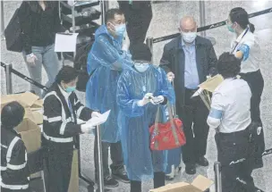  ??  ?? WE’RE WATCHING YOU: A photo taken through thick glass shows passengers wearing protective gear after receiving quarantine tracking wristbands at Hong Kong’s internatio­nal airport on Thursday. Hong Kong authoritie­s began ordering all arrivals from overseas to wear electronic bracelets, connected to an app that marks people’s location during the 14-day self-quarantine.