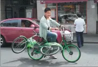  ?? GAO ERQIANG / CHINA DAILY ?? A man carries a public bicycle while riding another in Shanghai.