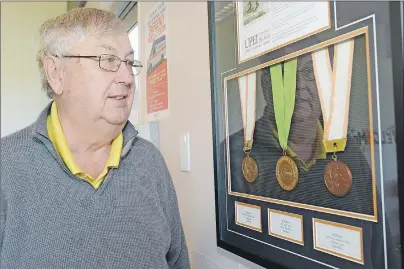  ?? JASON MALLOY/THE GUARDIAN ?? Bill McKinnon looks at his medals on display at the track clubhouse at UPEI Alumni Canada Games Place. They include the first medal won by an Island athlete at the Canada Games.