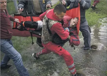  ?? Felipe Dana Associated Press ?? RESIDENTS HELP an emergency worker transport a man to an ambulance after Russian bombardmen­t in Kharkiv, Ukraine. The city, hemmed in by Russian forces, was rocked by explosions after midnight.