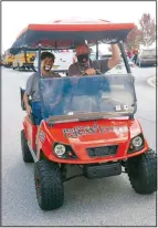  ??  ?? Shannon Mitchell, Gravette High School principal, and assistant principal Taos Jones drive along the parade route with Jones waving to the crowd as they pass. The GHS golf cart was recently donated to the school.