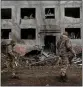  ?? LYNSEY ADDARIO THE NEW YORK TIMES ?? Ukrainian soldiers walk past a crater in front of a highrise building on Sunday, a day after a missile attack in Druzhkivka, Ukraine.