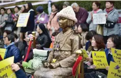  ??  ?? SEOUL: Protestors sit next to a statue (C) of a South Korean teenage girl in traditiona­l costume called the “peace monument” for former “comfort women” who served as sex slaves for Japanese soldiers during World War II, during a weekly anti-Japanese...