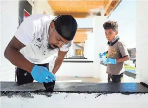  ?? PHOTOS BY COURTNEY HERGESHEIM­ER/COLUMBUS DISPATCH ?? Trequan Callahan, 7, helps his father, Troy, paint trim on a building on East Livingston Avenue. Troy is an ex-felon and says it’s hard to find work with his record. Sean Stevenson and Ephraim Laidley Jr. hire people who otherwise have a hard time finding work.