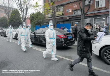  ?? Photos / AP : ?? Workers in protective clothing hit the streets as metal barriers are installed in Beijing.