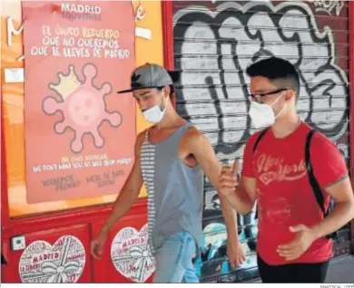  ?? MARISCAL / EFE ?? Dos jóvenes pasan ayer ante un cartel alusivo al coronaviru­s en el centro de Madrid.