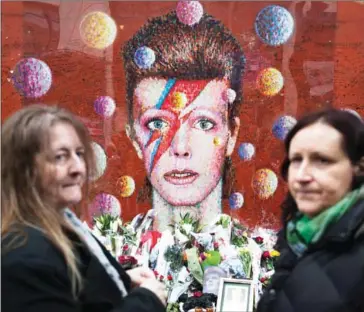  ??  ?? Fans gather in front of the mural of late British pop icon David Bowie created by Australian street artist James Cochran, also known as Jimmy C, as they pay their respects in Brixton, south London on January 10, 2017 on the first anniversar­y of Bowie’s...